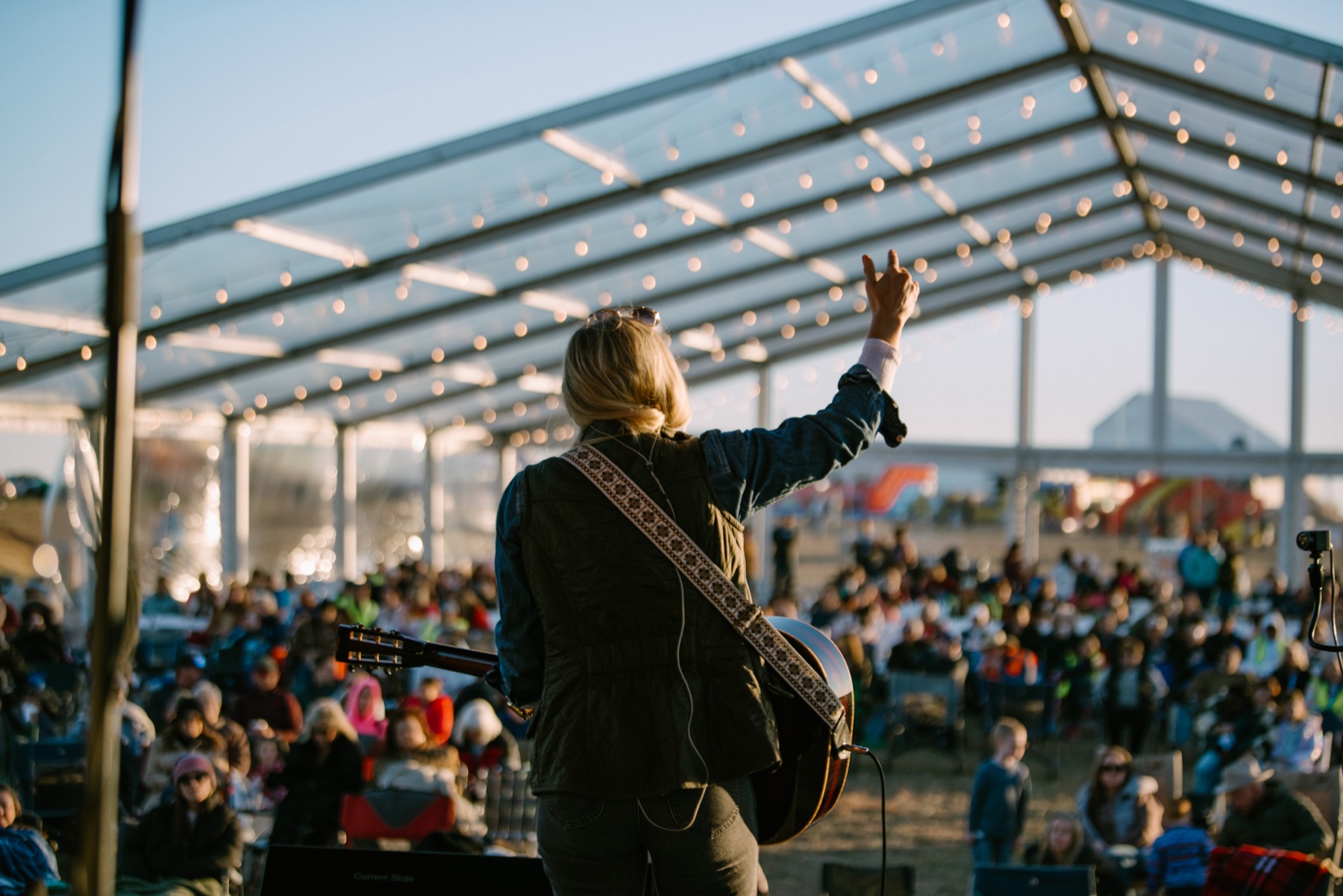 A worshipper on stage, crowd gathered in the golden evening light